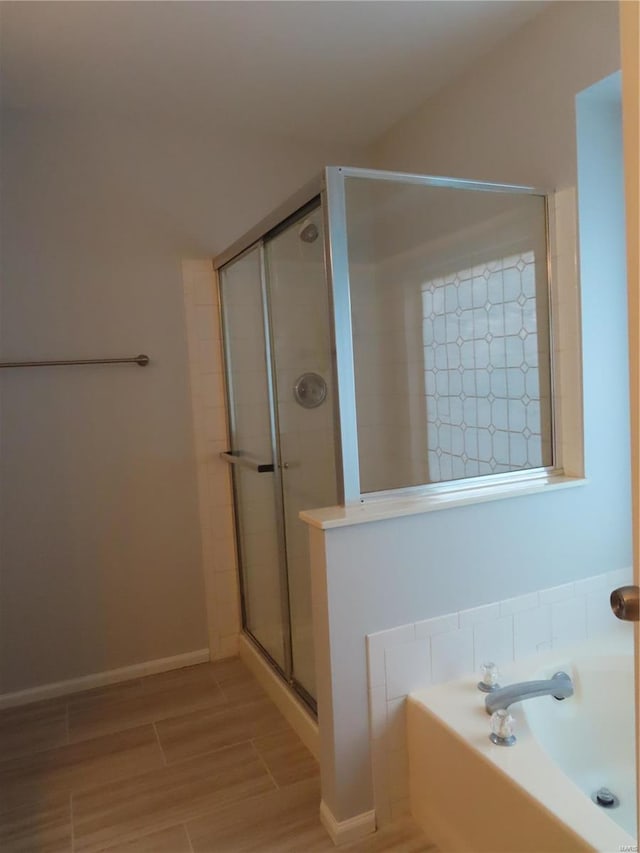 bathroom with a stall shower, wood tiled floor, baseboards, and a bath