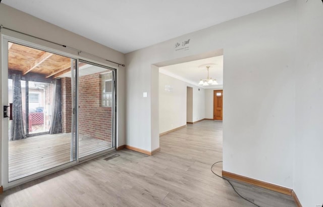 empty room featuring visible vents, wood finished floors, baseboards, and a chandelier