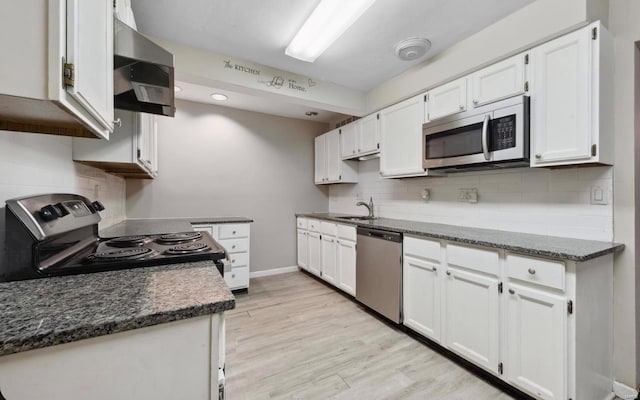 kitchen with stainless steel appliances, decorative backsplash, white cabinets, light wood-style floors, and wall chimney exhaust hood