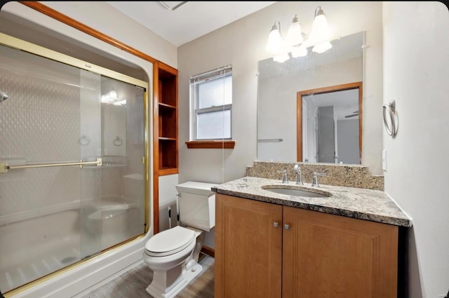 bathroom with vanity, toilet, wood finished floors, and a shower with shower door