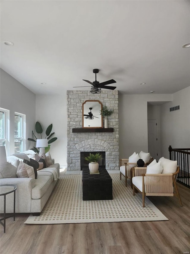 living room featuring a stone fireplace, wood finished floors, visible vents, and a ceiling fan