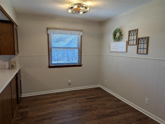 unfurnished dining area with a wainscoted wall, visible vents, and dark wood finished floors