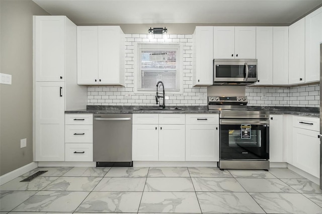 kitchen featuring dark countertops, marble finish floor, stainless steel appliances, and a sink