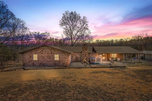 view of front of property with a yard, brick siding, a chimney, and a patio area