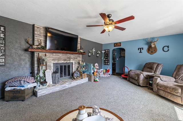 carpeted living area featuring a textured ceiling, a fireplace, arched walkways, and a ceiling fan