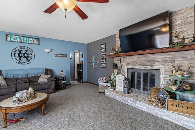 carpeted living area featuring arched walkways, a ceiling fan, a glass covered fireplace, a textured ceiling, and baseboards