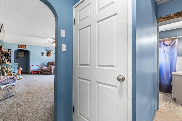 hall with arched walkways, light colored carpet, and a textured ceiling