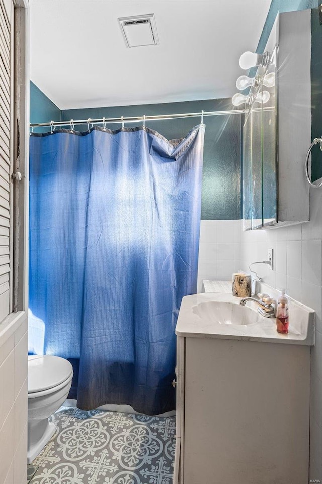 full bath featuring vanity, tile patterned flooring, visible vents, and tile walls