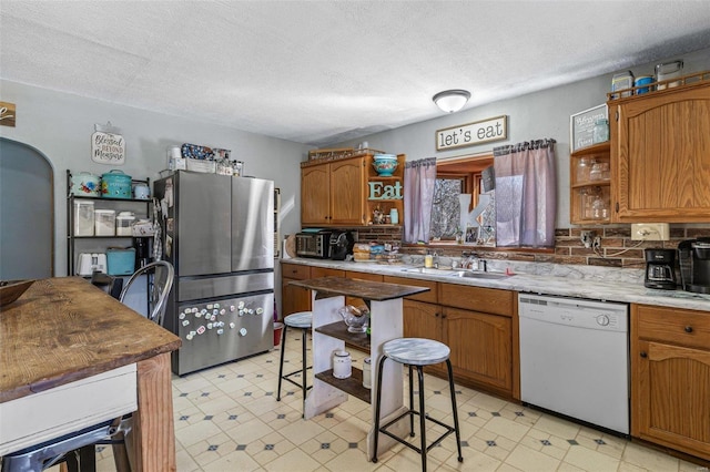 kitchen with light floors, a sink, freestanding refrigerator, dishwasher, and open shelves