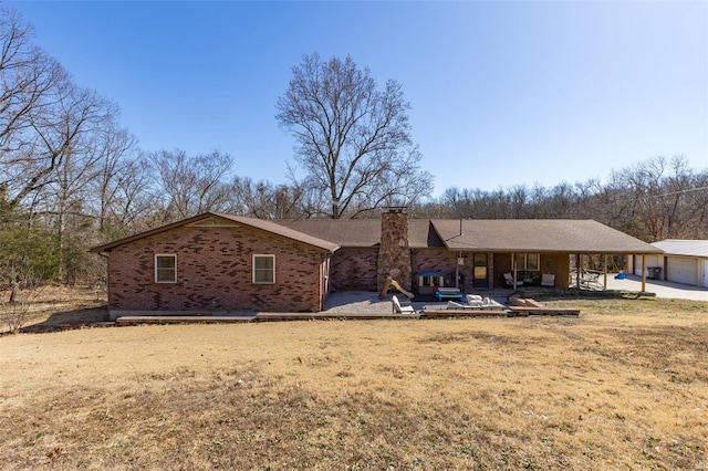 back of house with a yard, a patio, brick siding, and a chimney