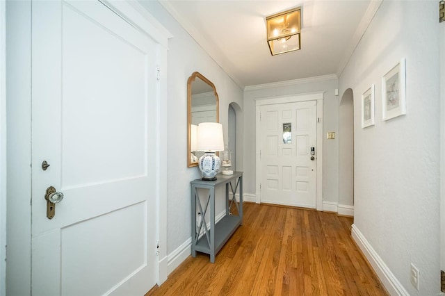 entrance foyer with arched walkways, crown molding, light wood-style flooring, and baseboards