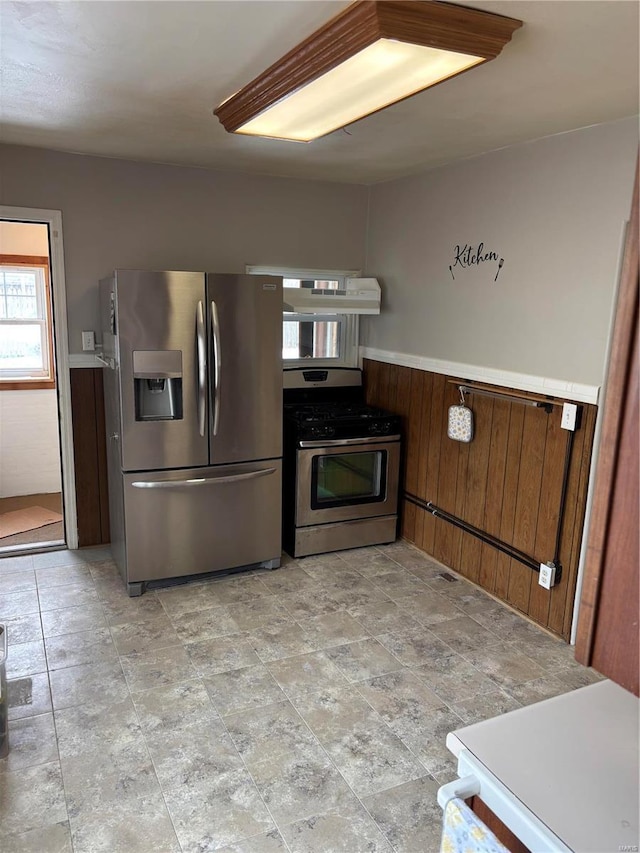 kitchen with a wainscoted wall, stainless steel appliances, wooden walls, and under cabinet range hood