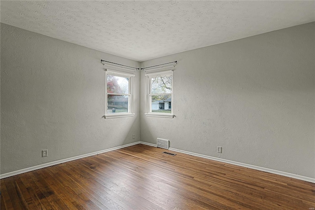 spare room with visible vents, a textured wall, a textured ceiling, wood finished floors, and baseboards