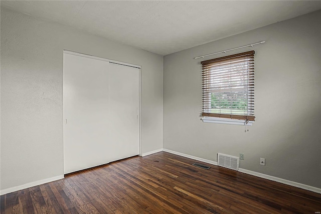 unfurnished bedroom featuring dark wood-style flooring, a closet, visible vents, and baseboards