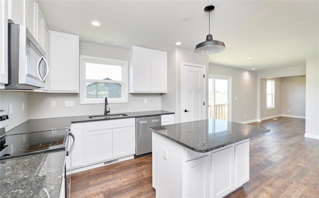 kitchen with white cabinets, a kitchen island, decorative light fixtures, stainless steel appliances, and a sink