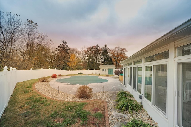 pool at dusk with a fenced in pool, a fenced backyard, an outdoor structure, and a storage unit