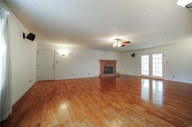 unfurnished living room with ceiling fan, french doors, a brick fireplace, and wood finished floors