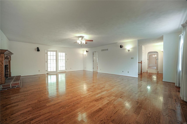 unfurnished living room with a brick fireplace, visible vents, arched walkways, and wood finished floors