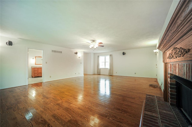 unfurnished living room featuring a brick fireplace, a ceiling fan, visible vents, and wood finished floors