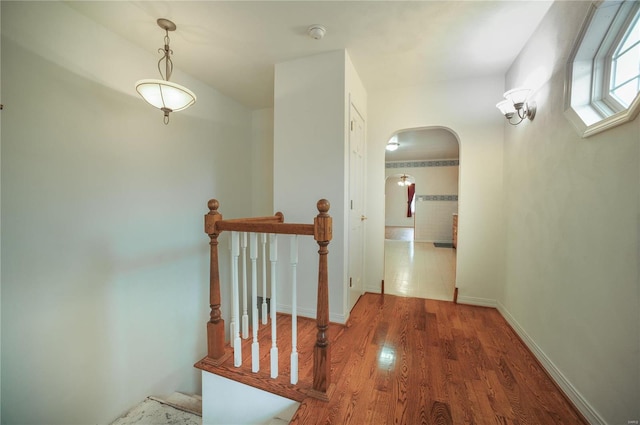 hallway featuring arched walkways, baseboards, and wood finished floors