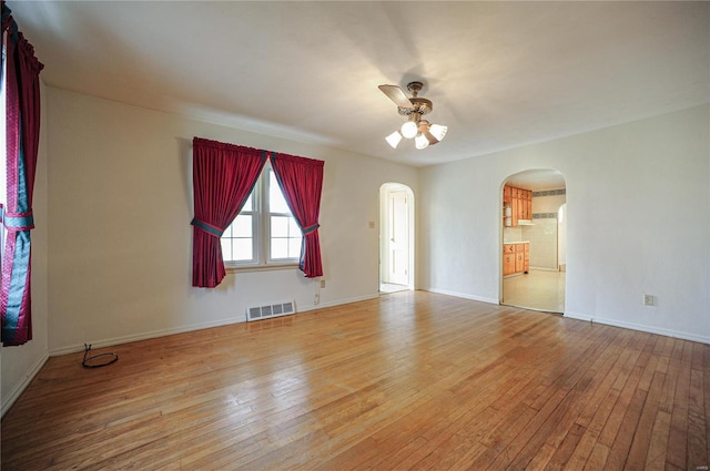 unfurnished room featuring arched walkways, a ceiling fan, baseboards, visible vents, and light wood-style floors