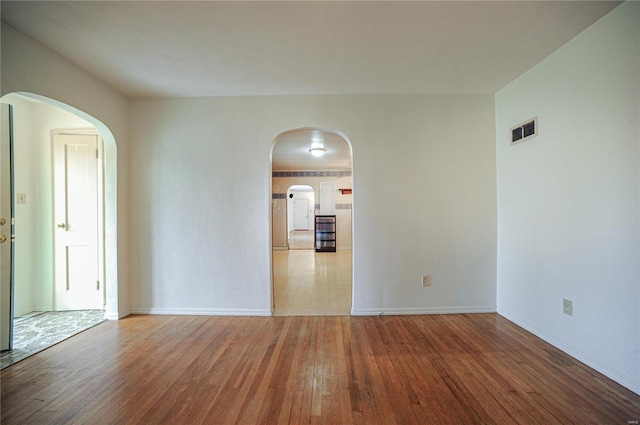 unfurnished room with arched walkways, visible vents, baseboards, and wood finished floors