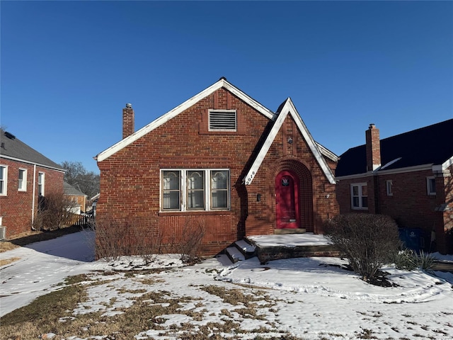 english style home featuring a chimney and brick siding