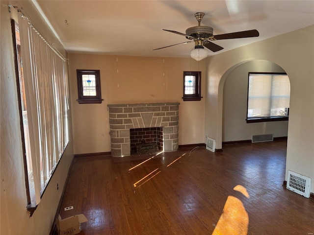 unfurnished living room with arched walkways, a fireplace, dark wood finished floors, and visible vents