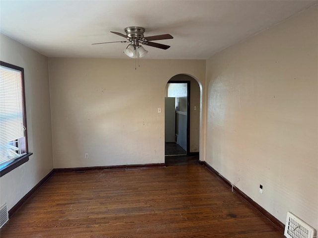 spare room featuring dark wood-type flooring, arched walkways, visible vents, and baseboards