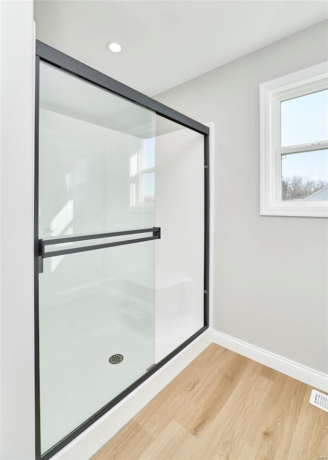 full bath with a shower with shower door, wood finished floors, visible vents, and baseboards