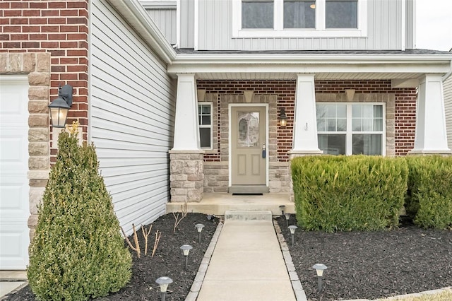 doorway to property featuring board and batten siding, covered porch, brick siding, and an attached garage