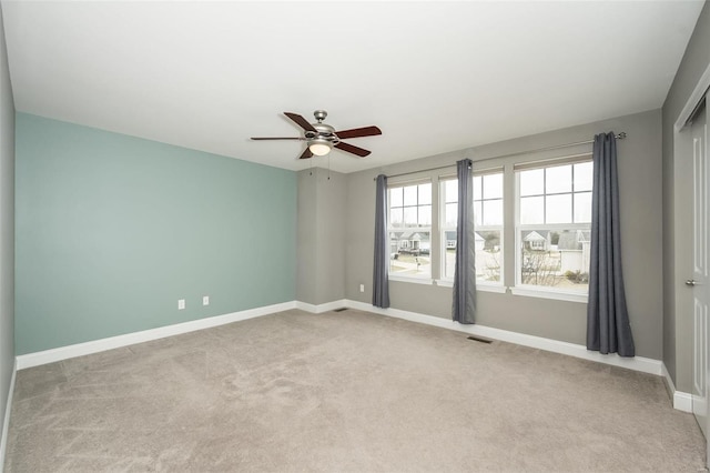 empty room with baseboards, visible vents, a ceiling fan, and light colored carpet