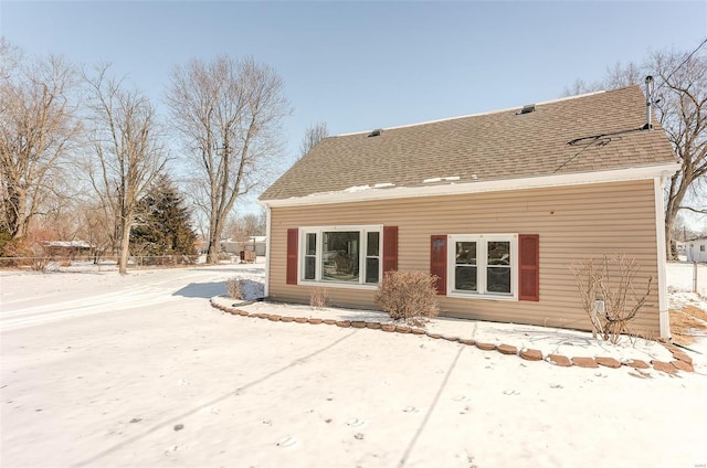 snow covered rear of property with a shingled roof