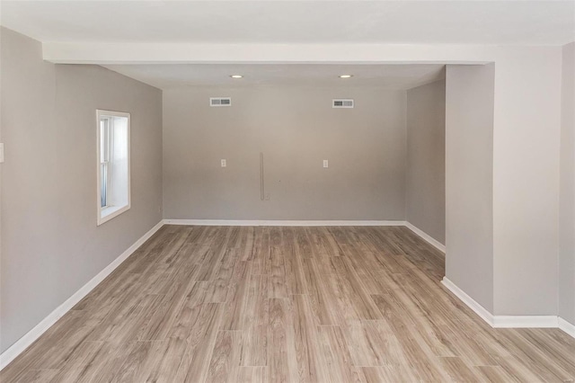 empty room with light wood finished floors, baseboards, visible vents, and beam ceiling