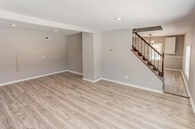 empty room with stairway, light wood-type flooring, visible vents, and baseboards