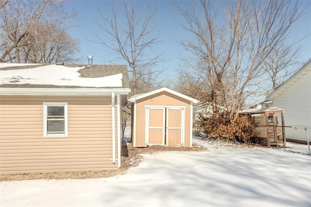 snow covered structure with an outbuilding, a storage unit, and fence