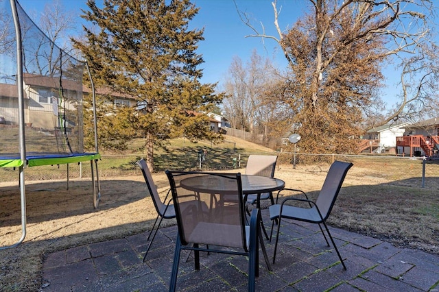 view of patio with a trampoline, fence, and outdoor dining space