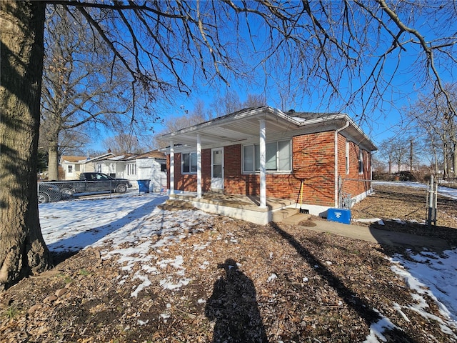 view of snow covered exterior featuring brick siding and fence