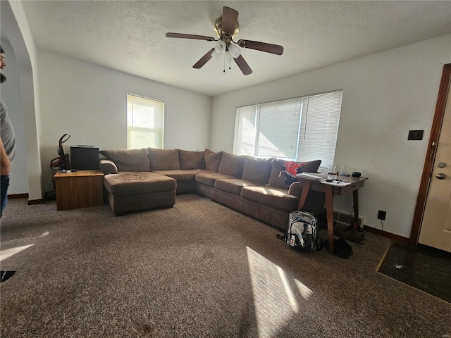 living area featuring ceiling fan, baseboards, dark carpet, and a textured ceiling