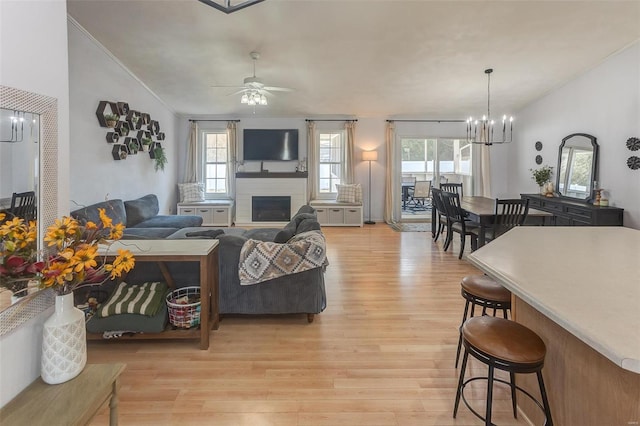 living room featuring light wood-style floors, vaulted ceiling, a fireplace, and ceiling fan with notable chandelier