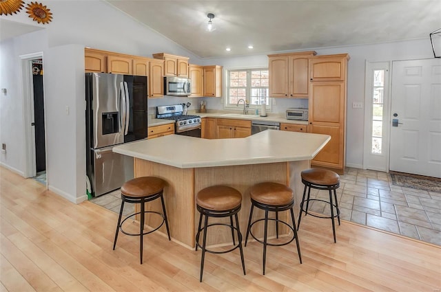 kitchen with appliances with stainless steel finishes, lofted ceiling, a sink, and a breakfast bar area