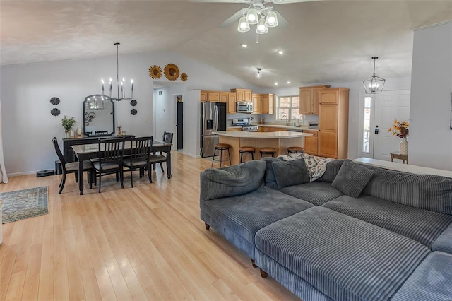 living room featuring lofted ceiling, light wood finished floors, and ceiling fan with notable chandelier