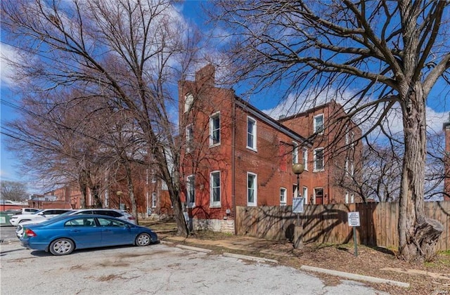 view of side of property featuring a chimney, fence, uncovered parking, and brick siding