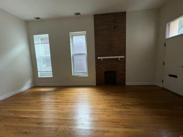 unfurnished living room with a brick fireplace, wood finished floors, and baseboards