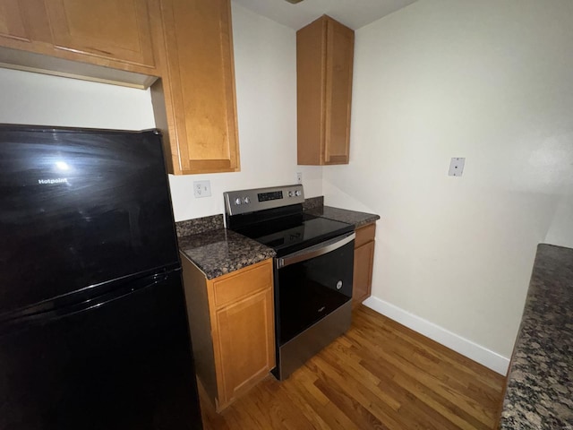 kitchen with wood finished floors, baseboards, stainless steel electric range, freestanding refrigerator, and dark stone countertops