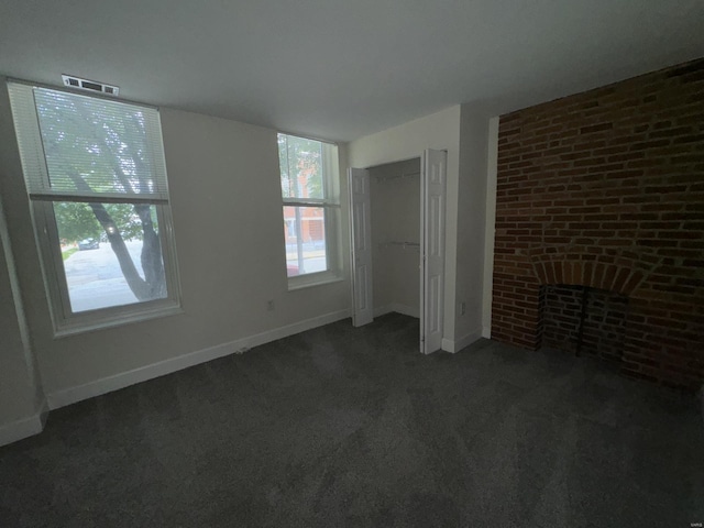 unfurnished bedroom with baseboards, visible vents, brick wall, a brick fireplace, and dark carpet