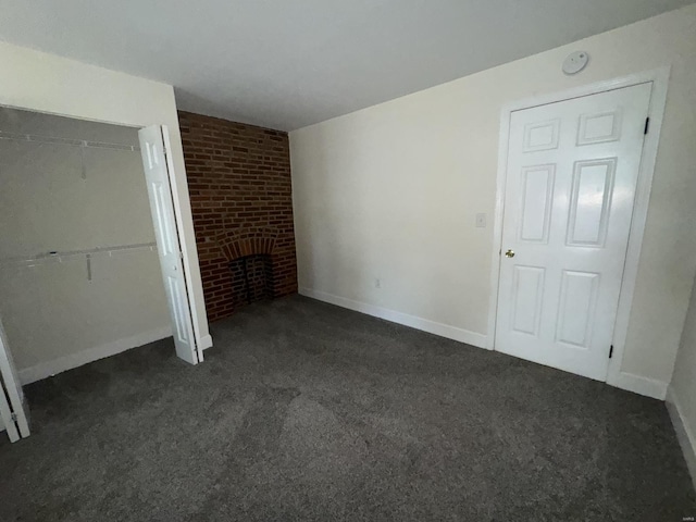 unfurnished bedroom with a closet, a brick fireplace, dark carpet, and baseboards