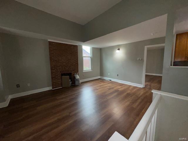 unfurnished living room featuring lofted ceiling, a fireplace, wood finished floors, and baseboards