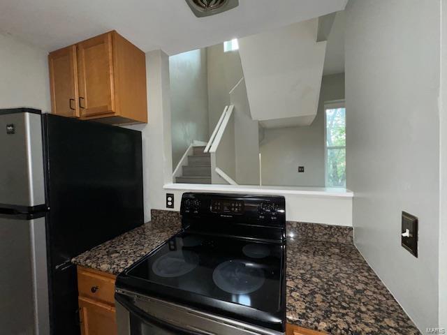 kitchen featuring brown cabinetry, black range with electric cooktop, dark stone counters, and freestanding refrigerator