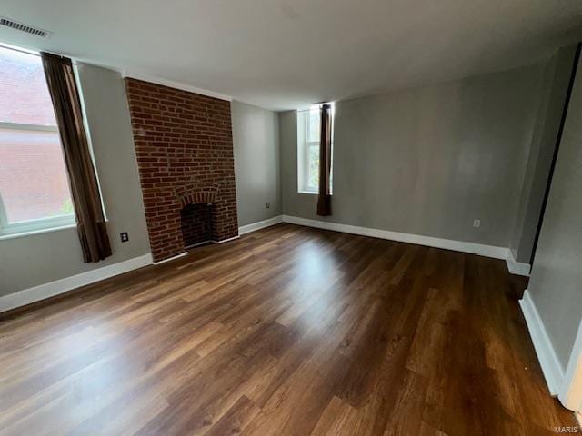 unfurnished living room featuring a brick fireplace, wood finished floors, visible vents, and baseboards